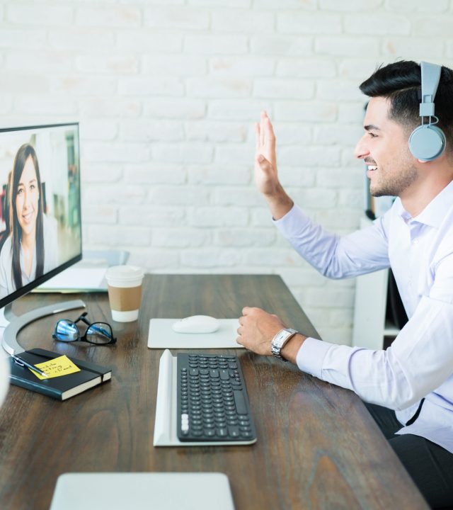 Confident young salesman waving at colleague during video call on computer at desk